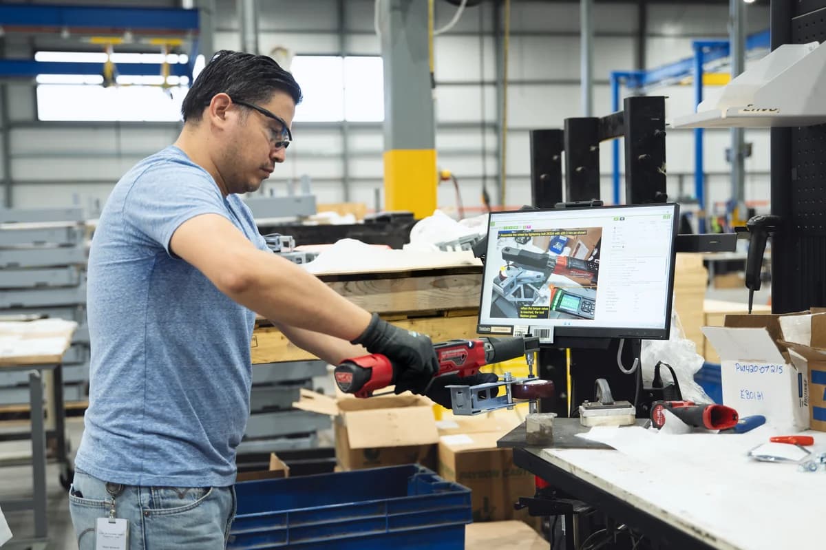 Opérateur en t-shirt gris utilisant un outil de serrage intelligent connecté à un écran VKS installé à côté de lui.