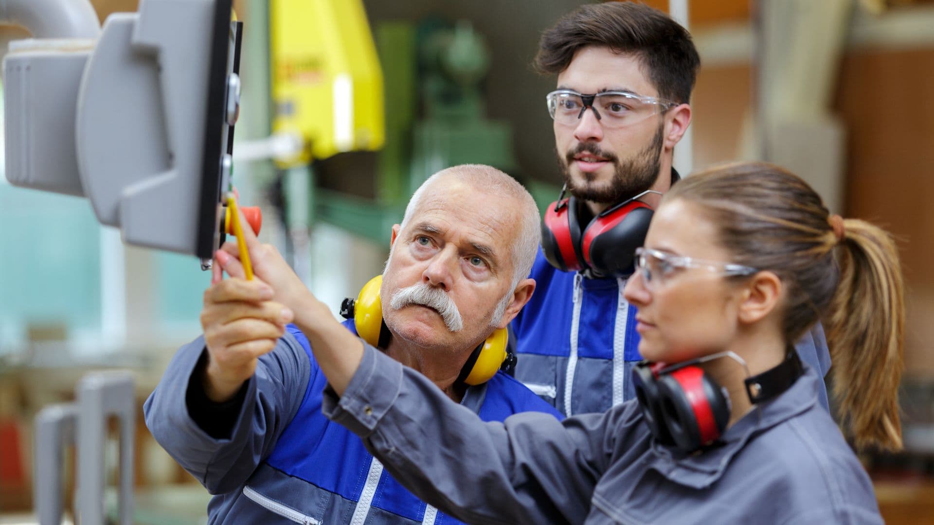 three factory workers looking at a screen and one of them press a button