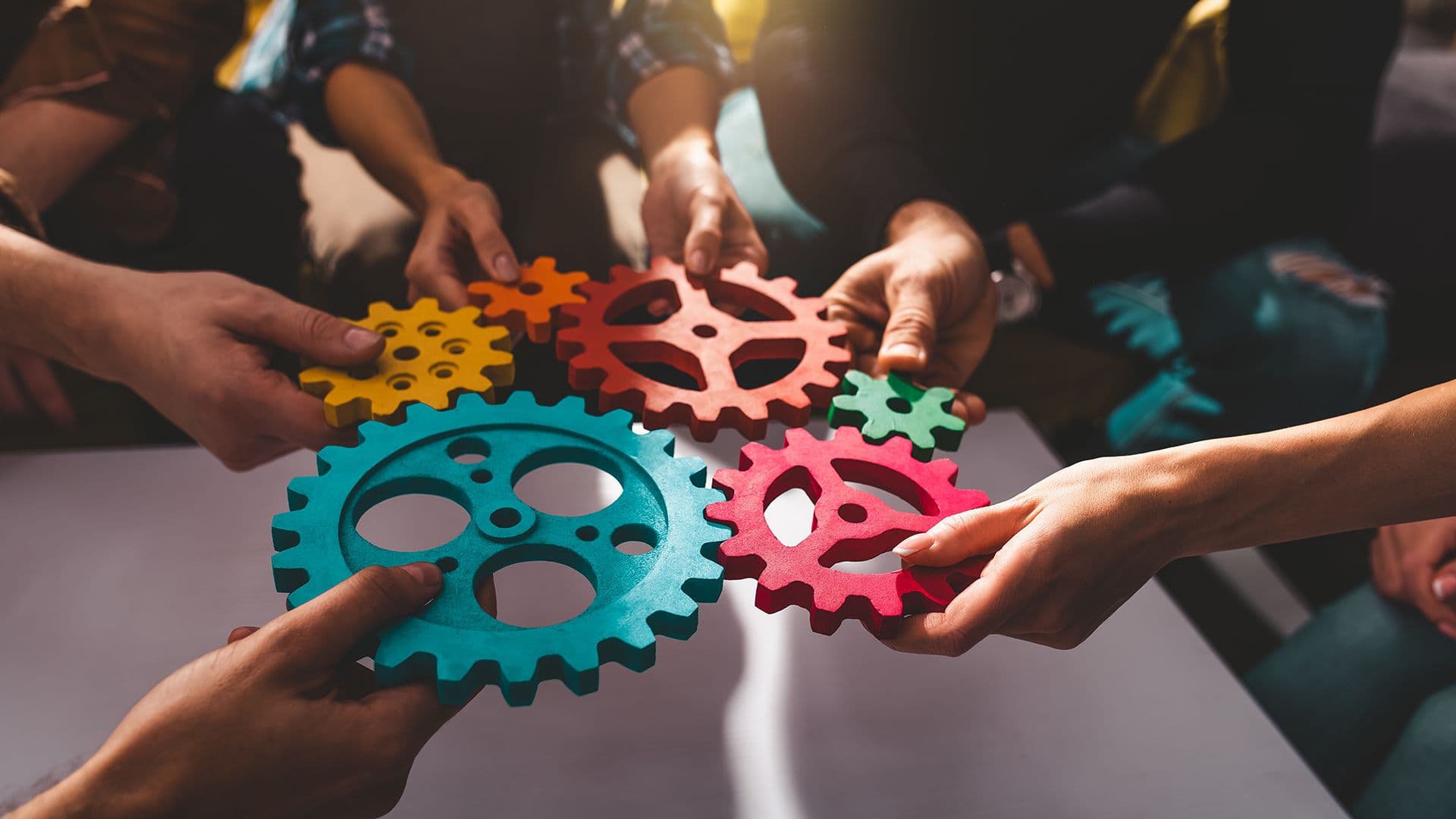 6 hands holding and putting together colored cogwheels