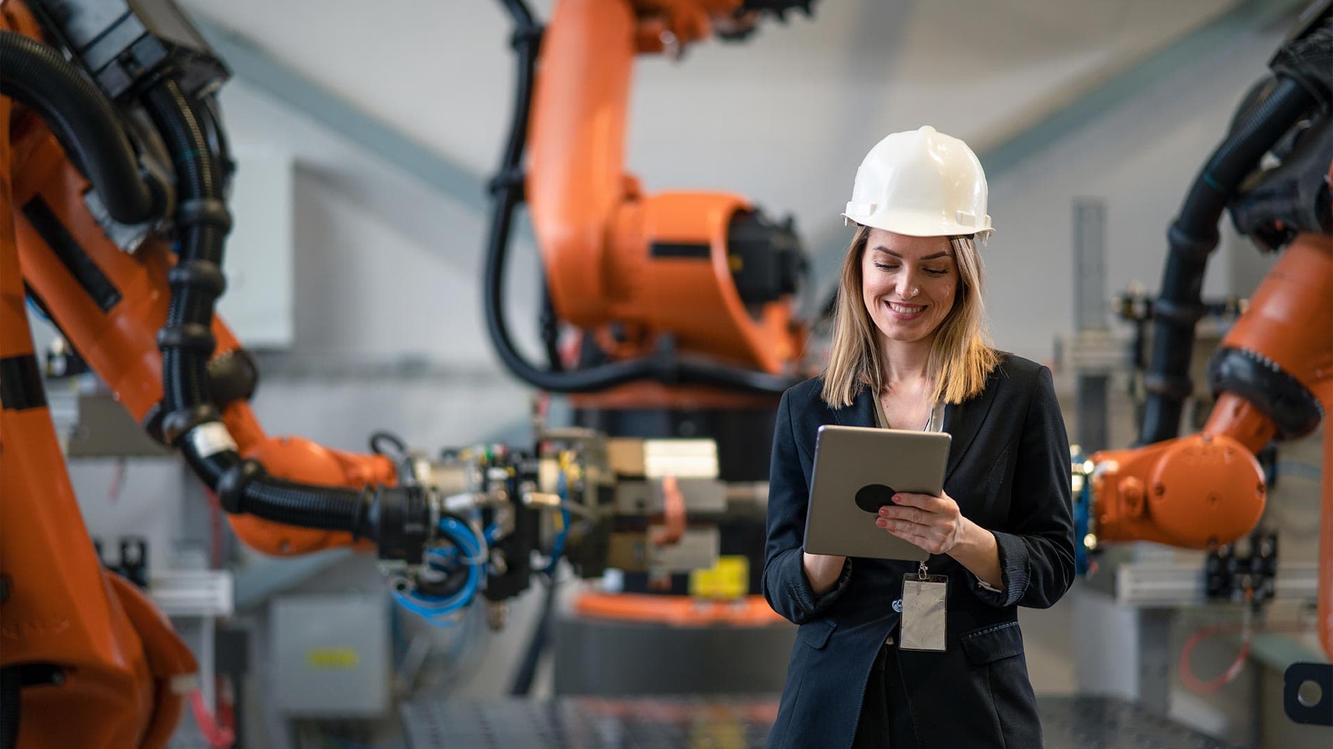 A woman wearing a hard hat standing next to robotic arms