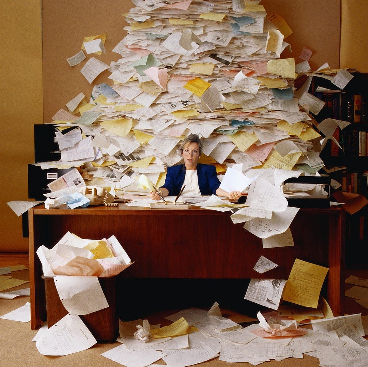 business woman sits at desk covered in loose leaf sheets of paper