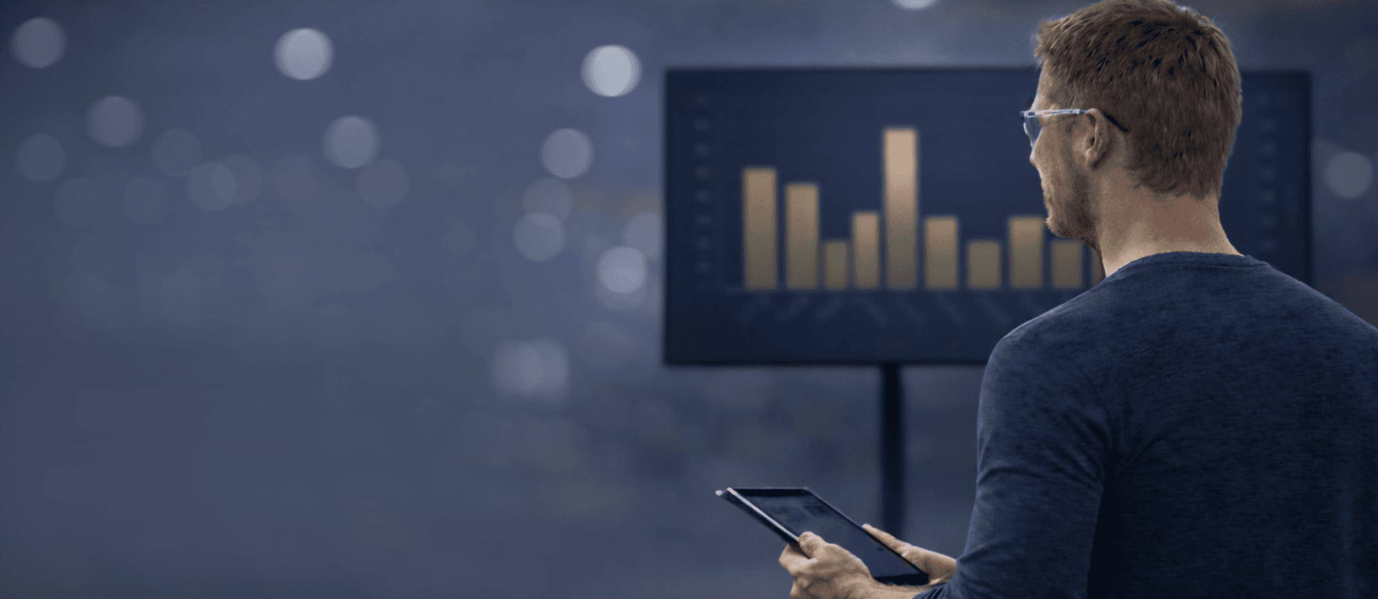 A supervisor looking at VKS KPIs on a large screen while holding a tablet