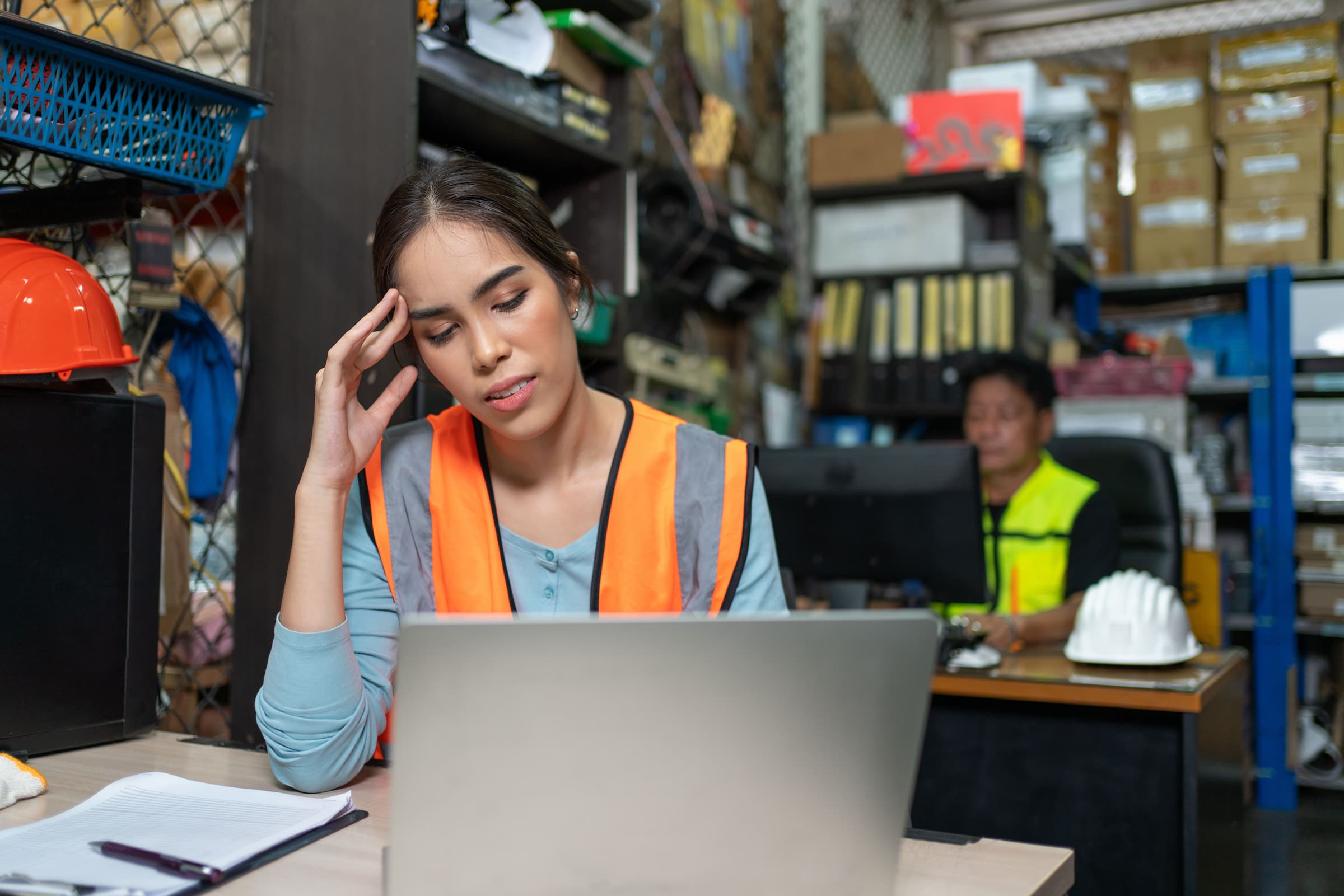 woman in safety vest looks at computer in frustration