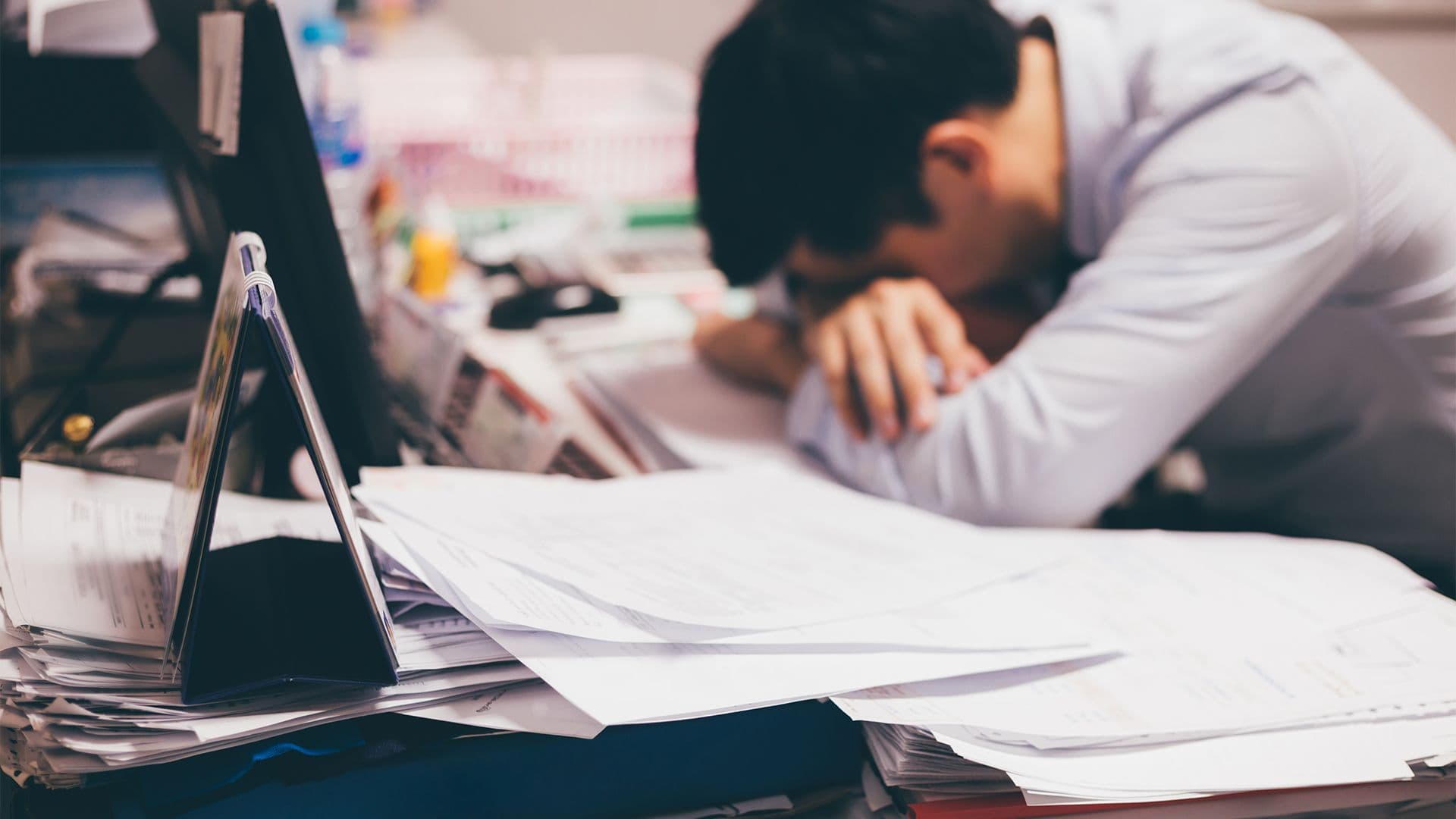 Man sitting down and sleeping with head on his hands over the desk