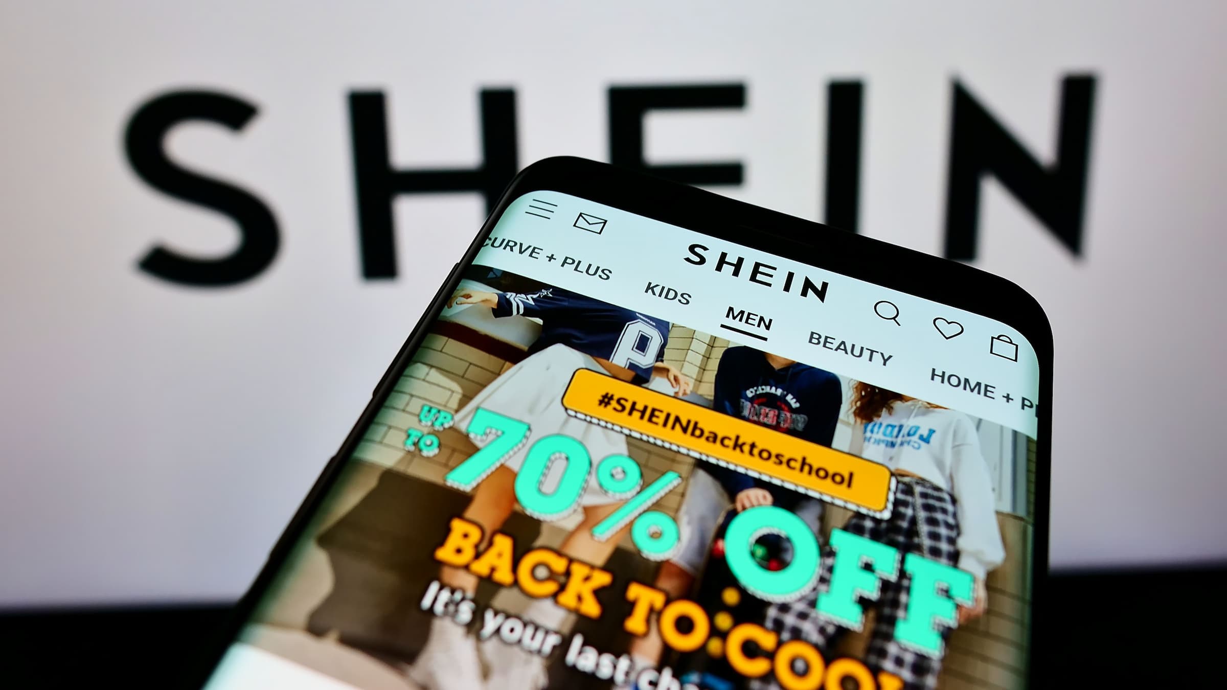 cellphone open to Shein mobile app in front of Shein logo in background